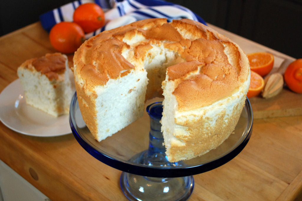 Tall gluten-free angel food cake on a cake stand with a golden crust