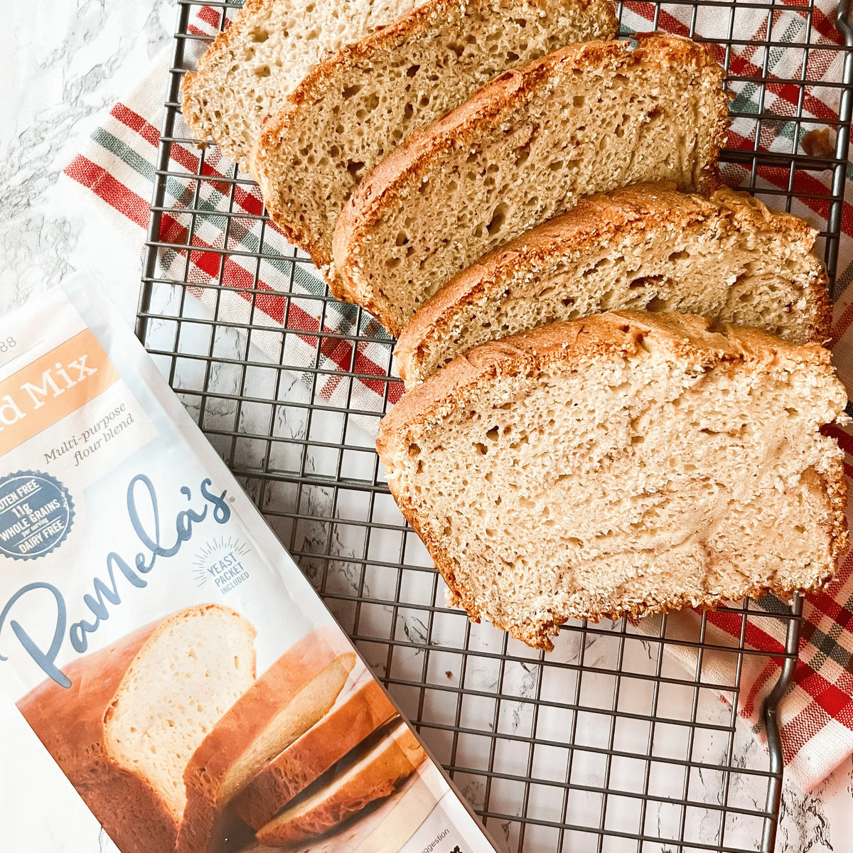 Sliced loaf of bread on a cooling rack with Pamela's Bread Mix packaging.