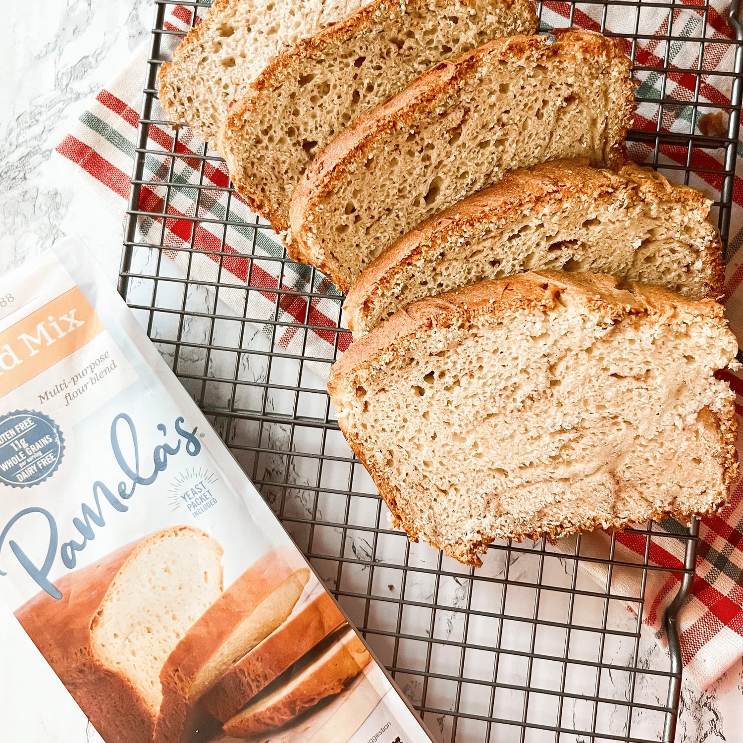 Sliced loaf of bread on a cooling rack with Pamela's Bread Mix packaging.