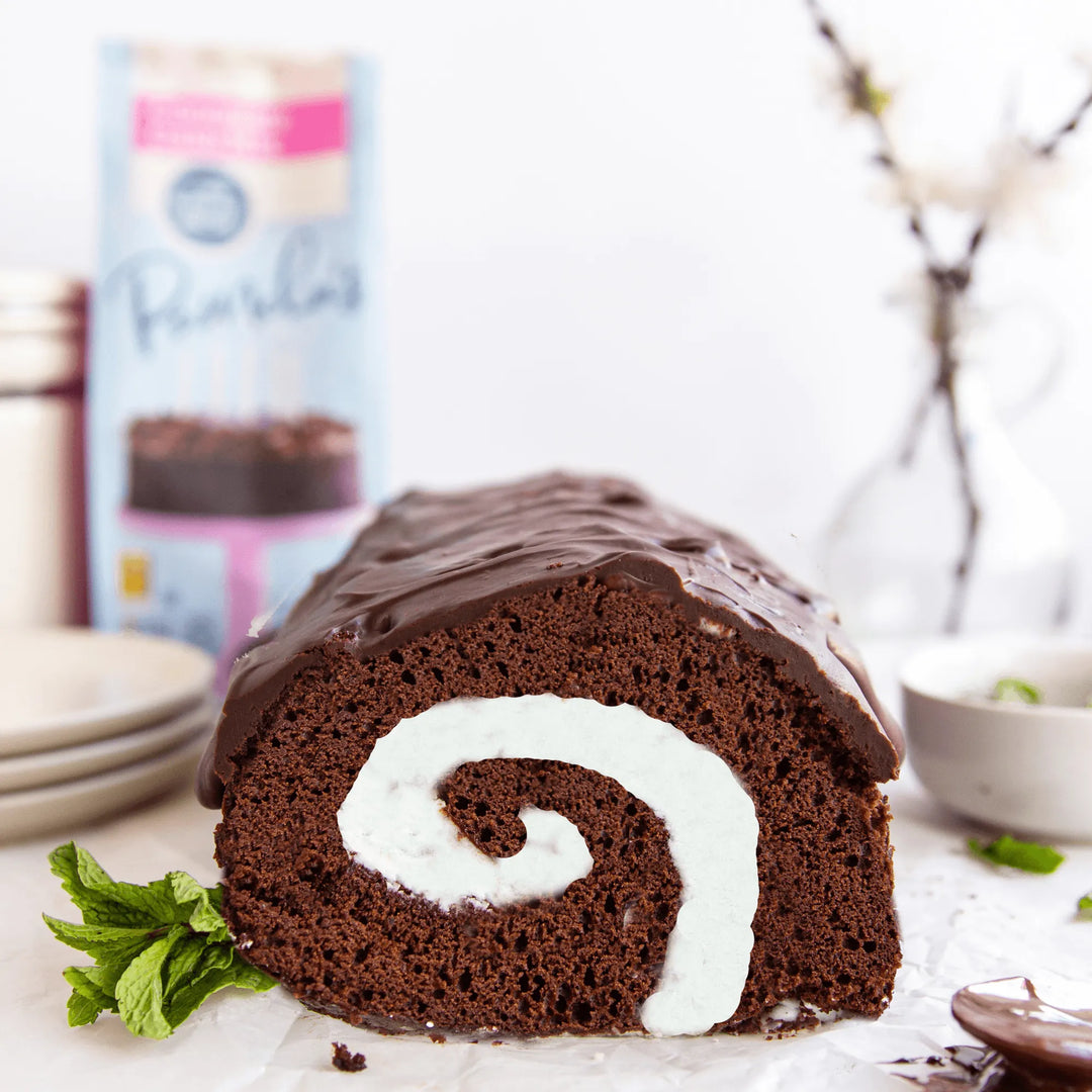 Chocolate cake roll with white cream filling on a marble surface, with a blurred background.