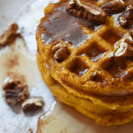 Stack of pumpkin waffles with syrup and pecans on a white plate