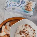 Box of Pamela's gluten-free bread on a marble surface with a bowl of dessert and apple slices.