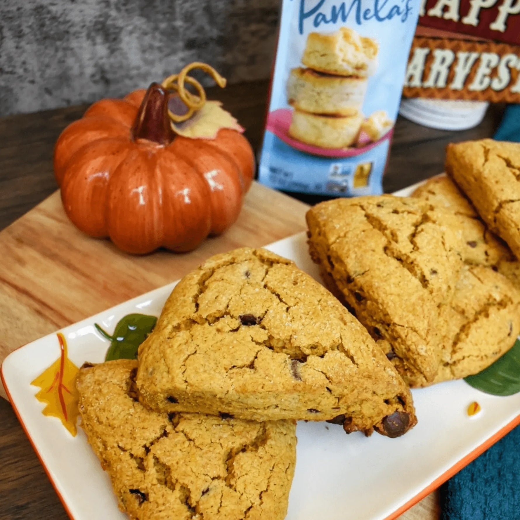 Pumpkin scones on a decorative plate with a pumpkin and baking powder container in the background.